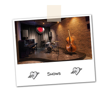 An empty stage with a piano, drums, cello and a mic.